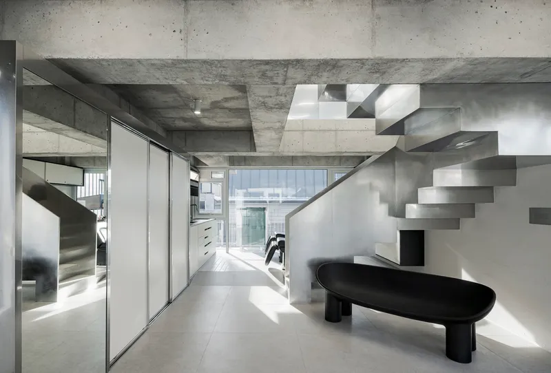 Interior view of the folded steel staircase rising against white walls beneath exposed concrete beams