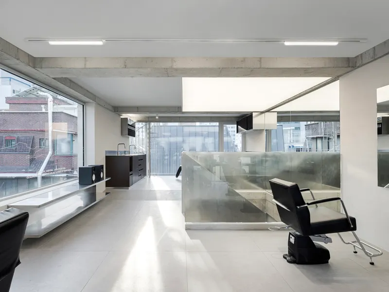 Open salon space with stainless steel partition walls and large windows overlooking neighboring buildings