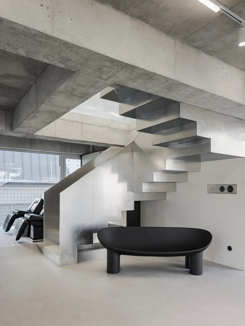 Close-up of the cantilevered steel staircase beside a low black table under concrete structure