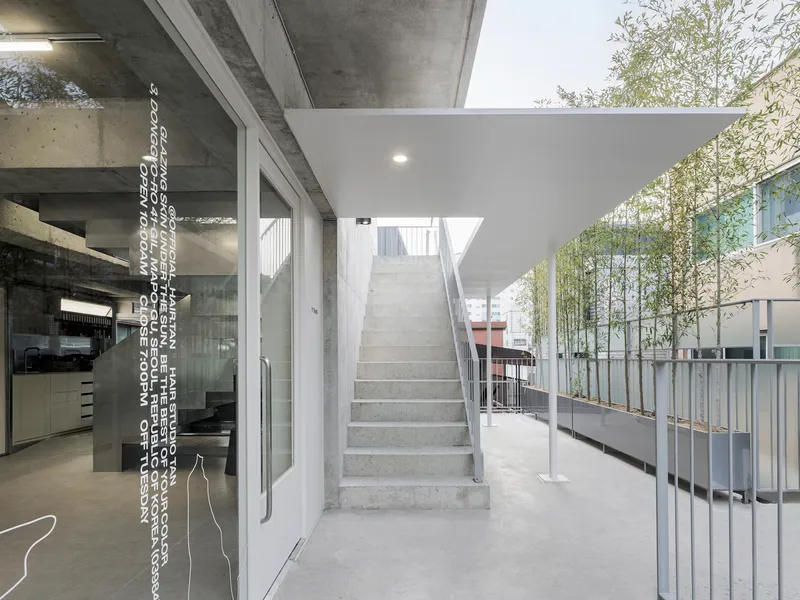Outdoor terrace with concrete staircase ascending beneath a canopy, adjacent to glass walls and bamboo plants