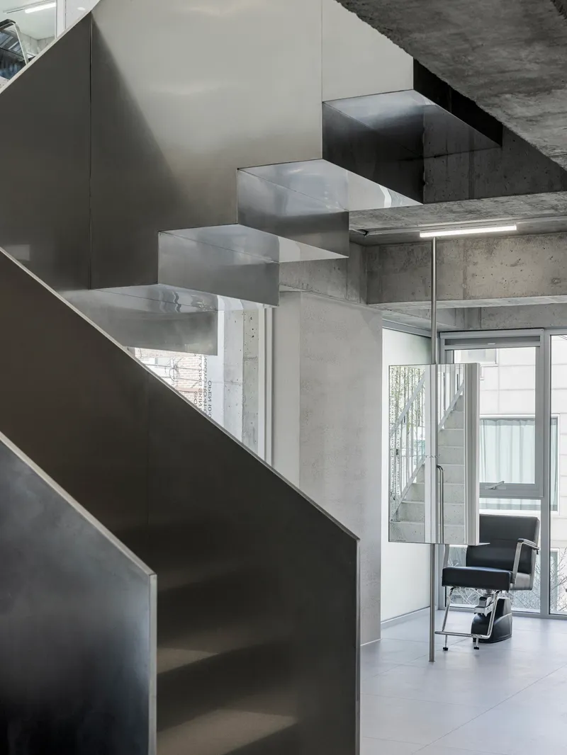 Steel staircase descending beside exposed concrete columns with a chair visible through the doorway
