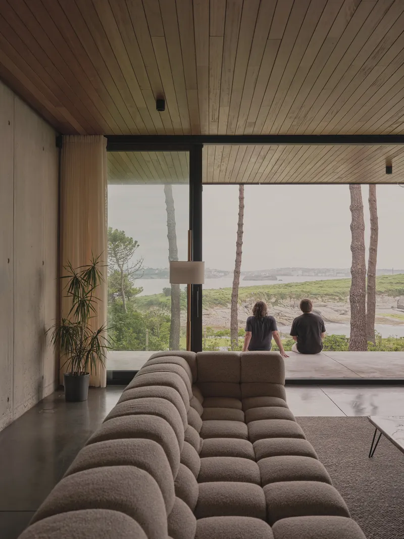 Interior view with two figures seated at the glazed wall looking out to coastal landscape