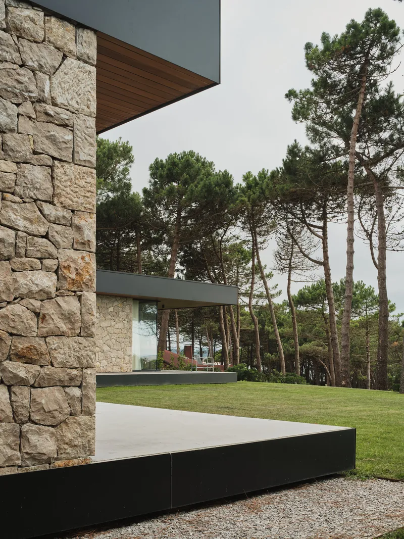 Stone tower with timber soffit and black plinth platform surrounded by pines and gravel
