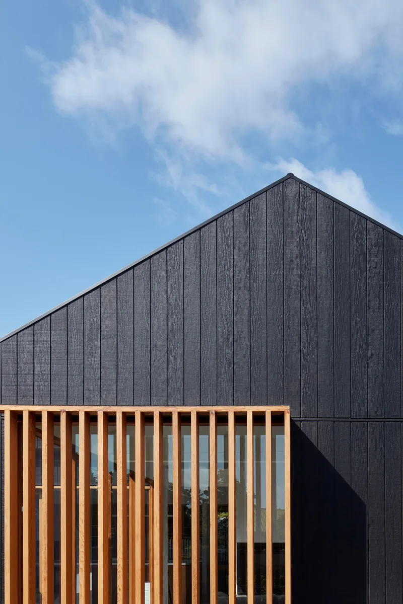 Close-up of the vertical timber screen against the black cladding beneath wispy clouds