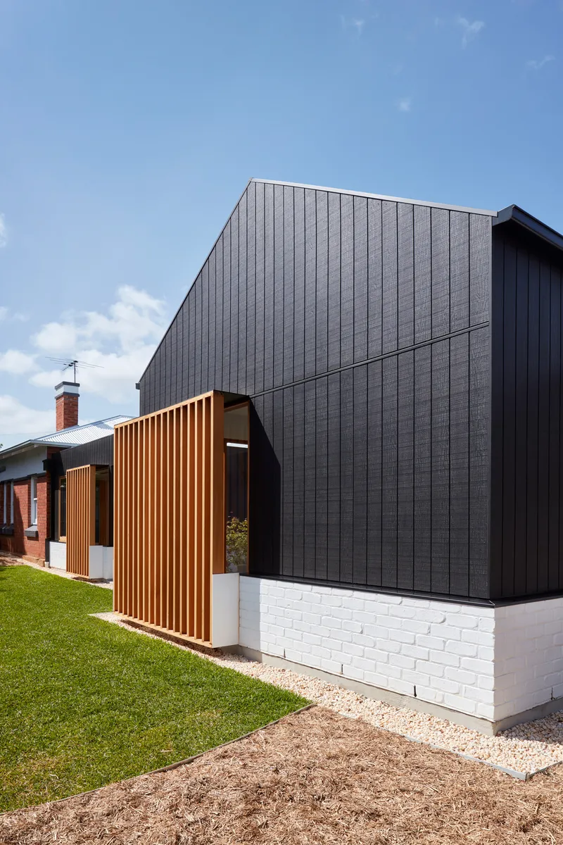 Street view showing the dark vertical cladding above a painted brick base with timber screen panels