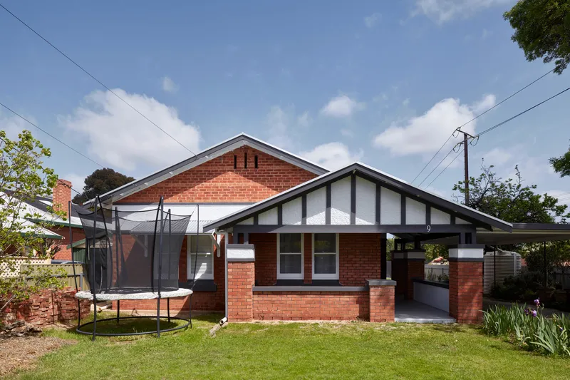 Gabled brick dwelling with a trampoline in the front lawn under scattered clouds