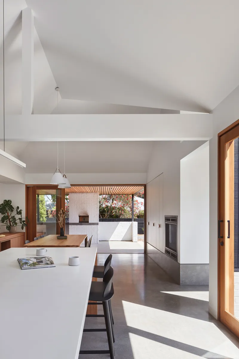 Open plan kitchen and dining area with high ceilings and sunlight streaming through timber framed doors