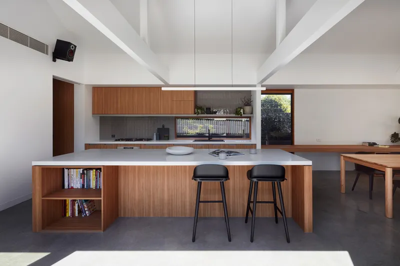 Kitchen island with timber cabinetry and white stone countertop beneath exposed white beams and clerestory skylights