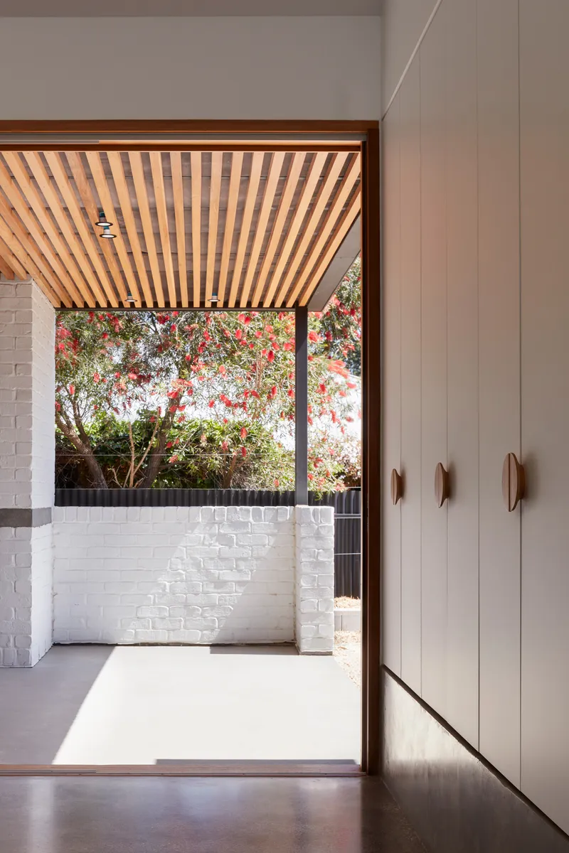 Doorway with timber batten ceiling opening to a white brick courtyard with flowering tree overhead