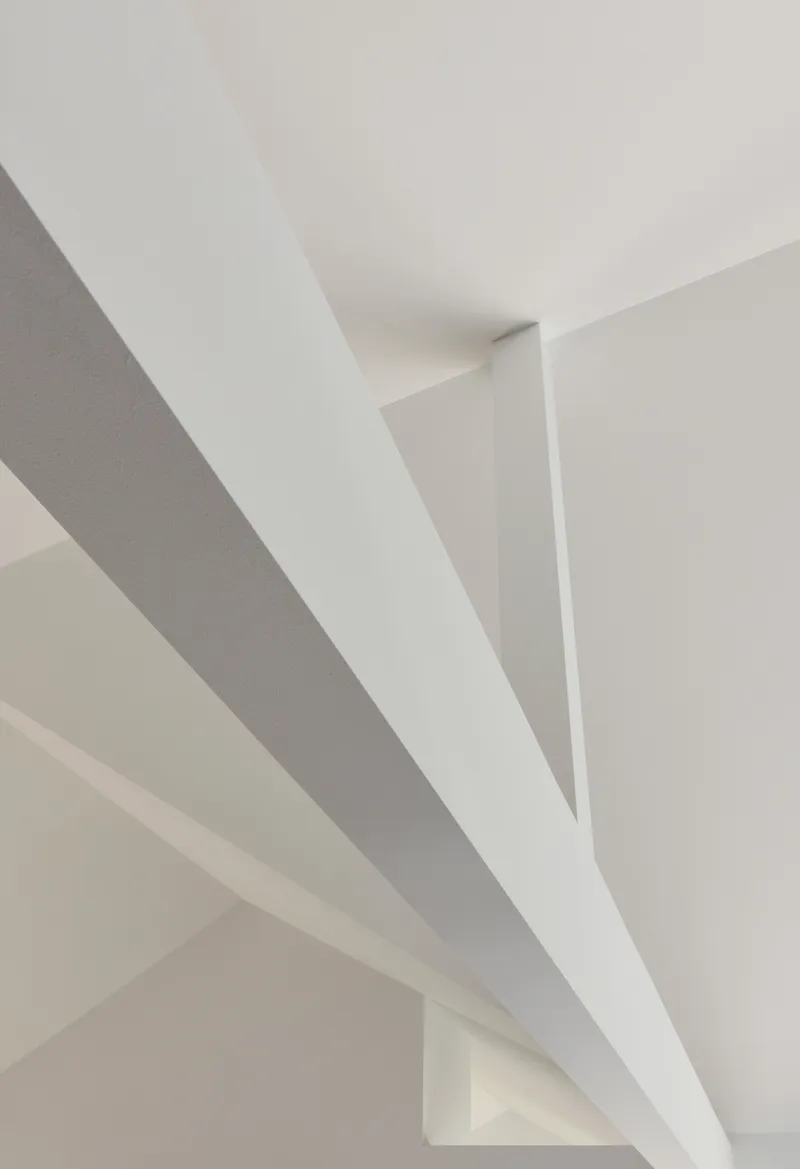 Ceiling detail showing white painted steel beams crossing at angles in soft daylight