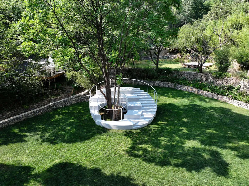 Curved outdoor staircase with white treads and tubular railings nestled among trees and stone walls