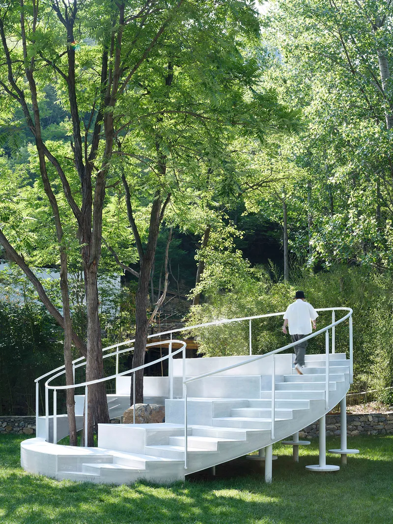 Person ascending the white spiral stair with open risers and tubular steel handrails