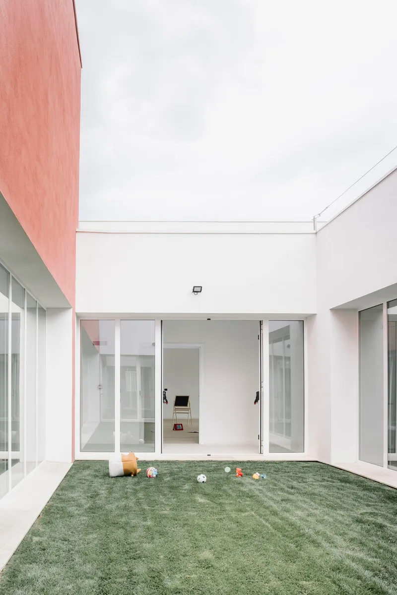 Internal courtyard with white walls, glazed doors and a striped lawn with scattered toys