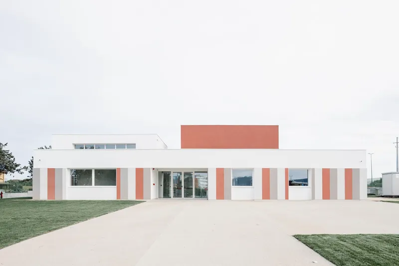 Frontal view of the white facade with terracotta vertical panels and a raised terracotta roof volume