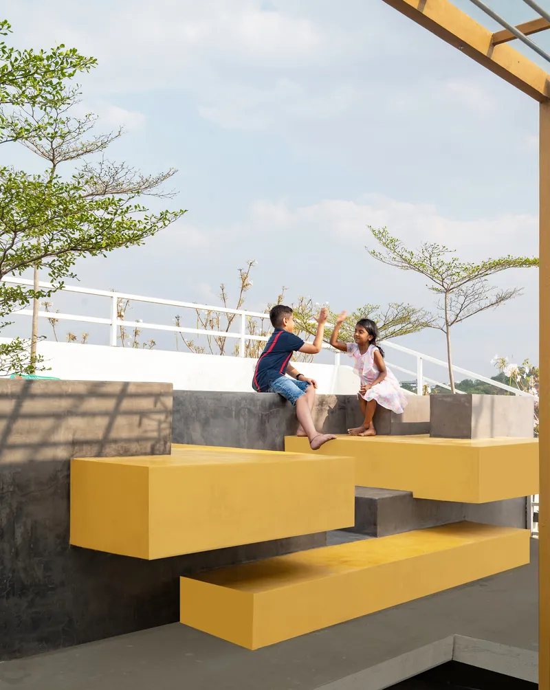 Cantilevered yellow steel stairs with two children playing under open sky and scattered clouds