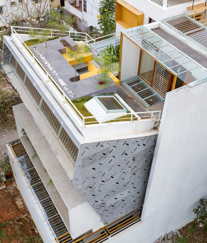 Aerial view of the multi-level residence with rooftop garden, yellow accents, and perforated courtyard paving