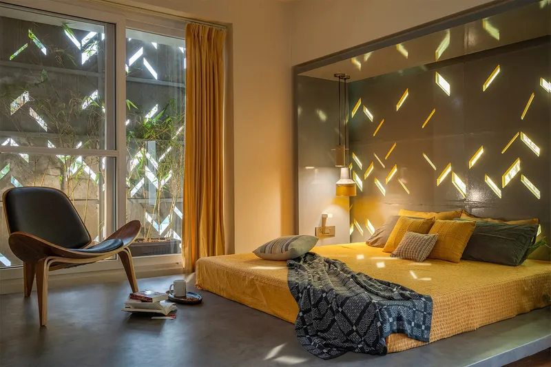Bedroom with perforated concrete wall casting dappled light patterns across the bed and polished floor