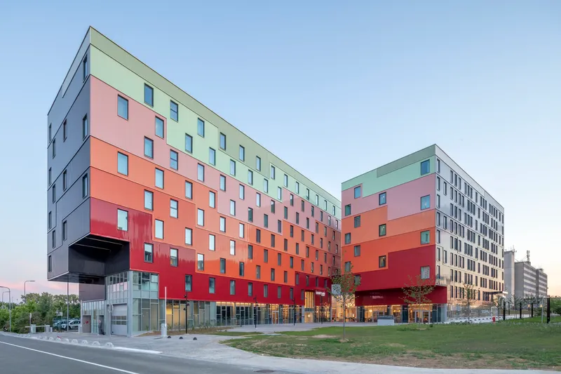 Gradient color panel facade transitioning from red to yellow to green beneath a pale evening sky