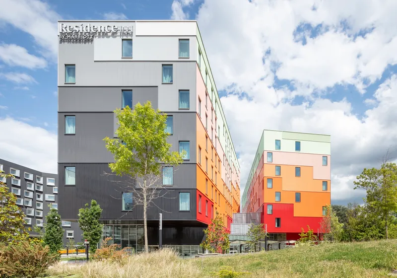 Two residential blocks with color-shifting facades separated by a narrow courtyard with young trees