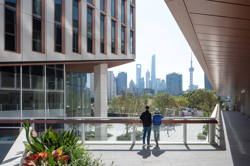 Elevated terrace with two visitors overlooking planted shrubs and distant skyline under hazy afternoon light