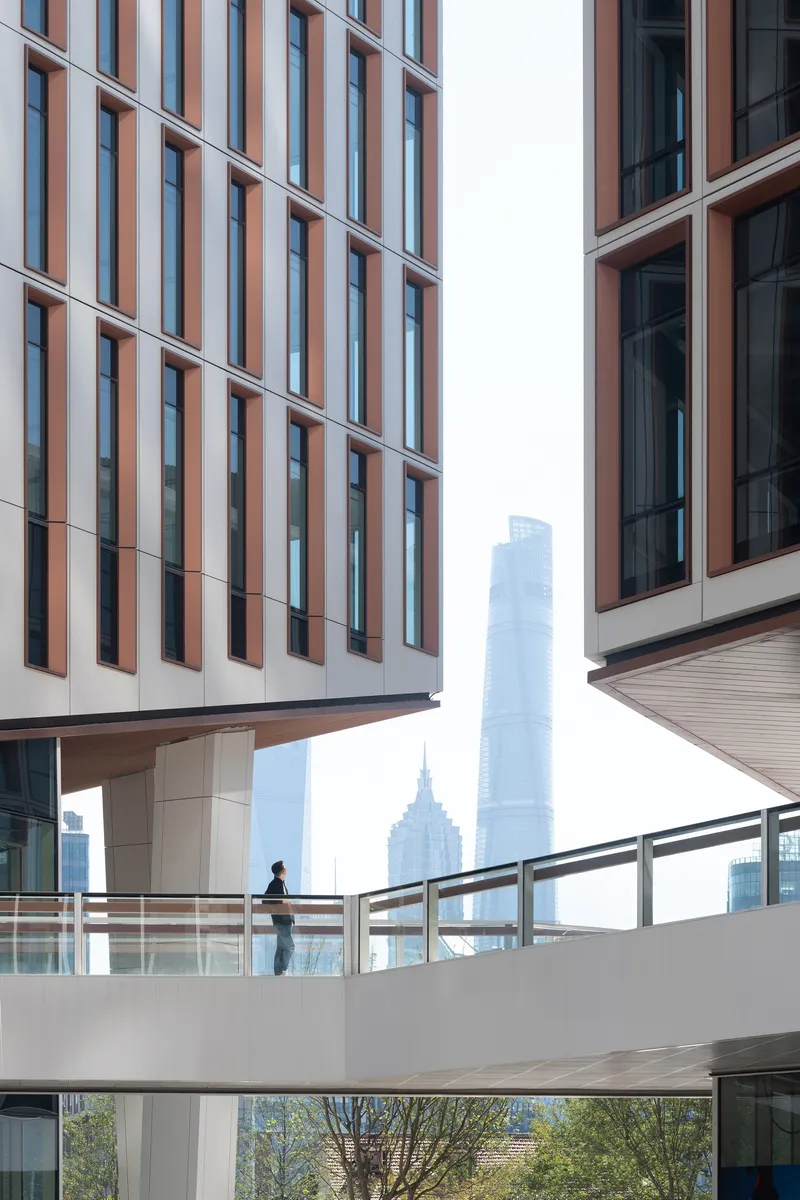 Elevated pedestrian bridge connecting two towers framed by vertical terracotta and white facade panels with distant skyline