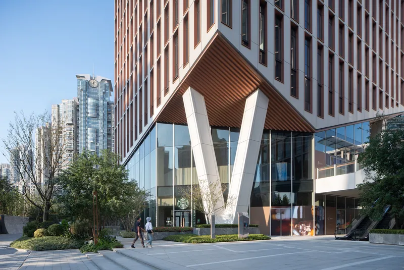 Entry pavilion with white diagonal columns and ribbed soffit anchoring a vertical terracotta-striped tower facade at dusk