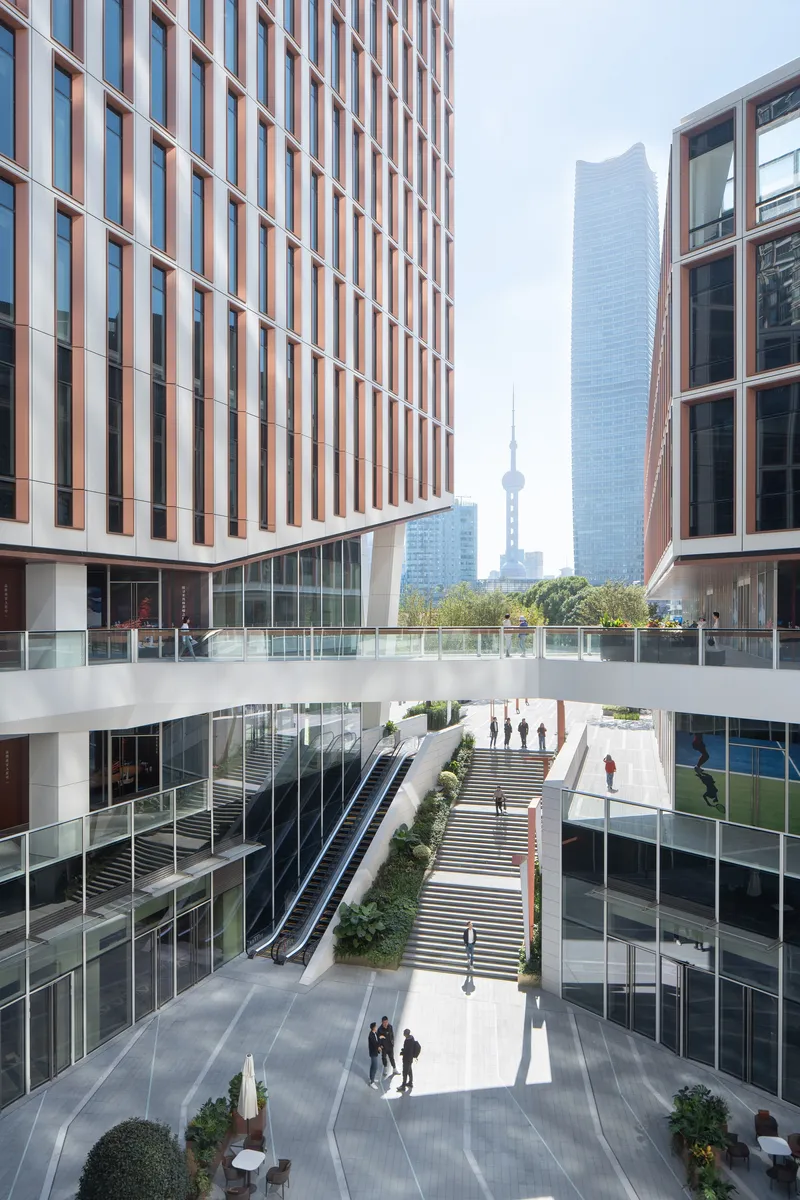 Sunken courtyard plaza with pedestrians and escalator between towers with vertical bronze fins
