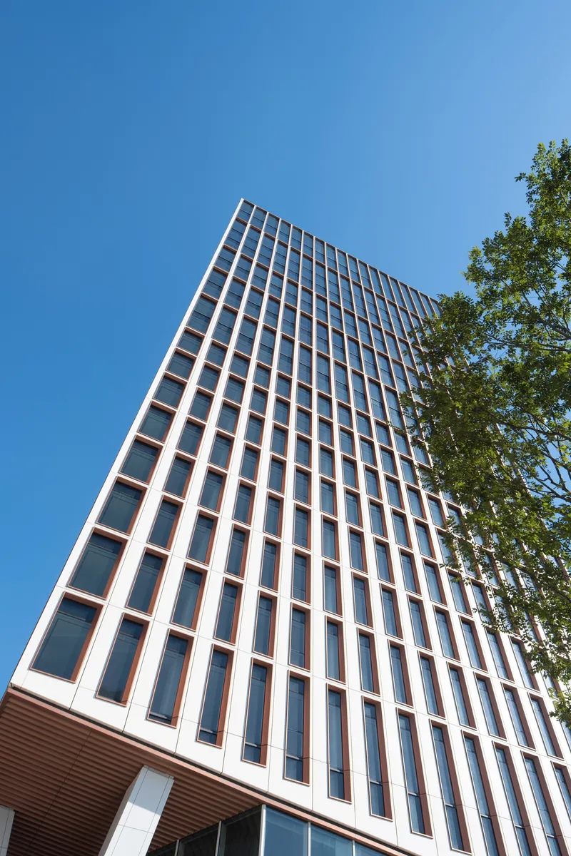 Upward view of the white panelized facade with bronze window frames against clear blue sky