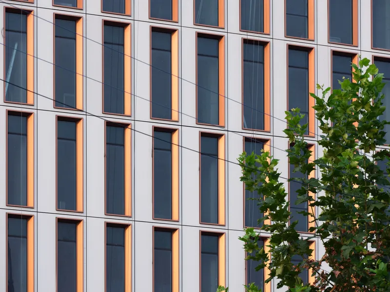 Close-up of the white facade panels with bronze window reveals and green street trees