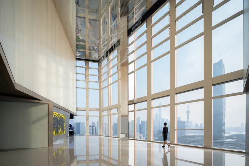 Double-height lobby space with floor-to-ceiling glazing and a figure silhouetted against the skyline