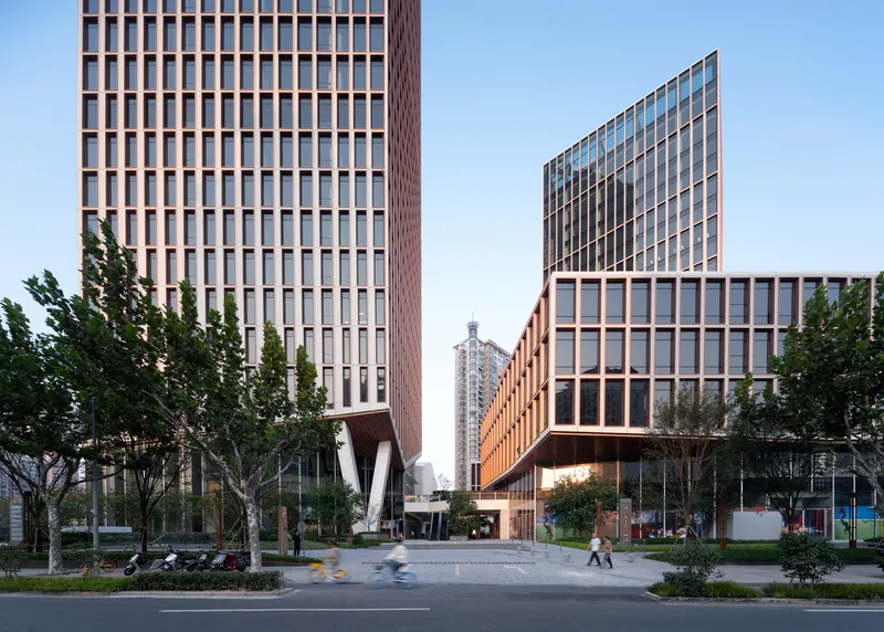 Street view of glazed tower facades flanking a ground-level entry with white V-shaped columns under clear sky