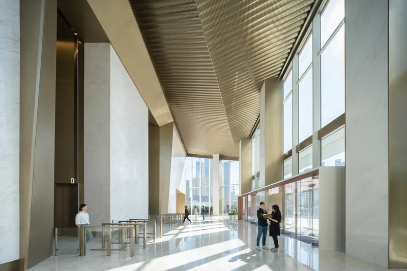 Interior lobby with ribbed metal ceiling soffit and stone-clad columns flooded with daylight