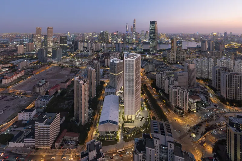 Aerial view of twin tower complex and curved podium within the dense urban fabric at twilight