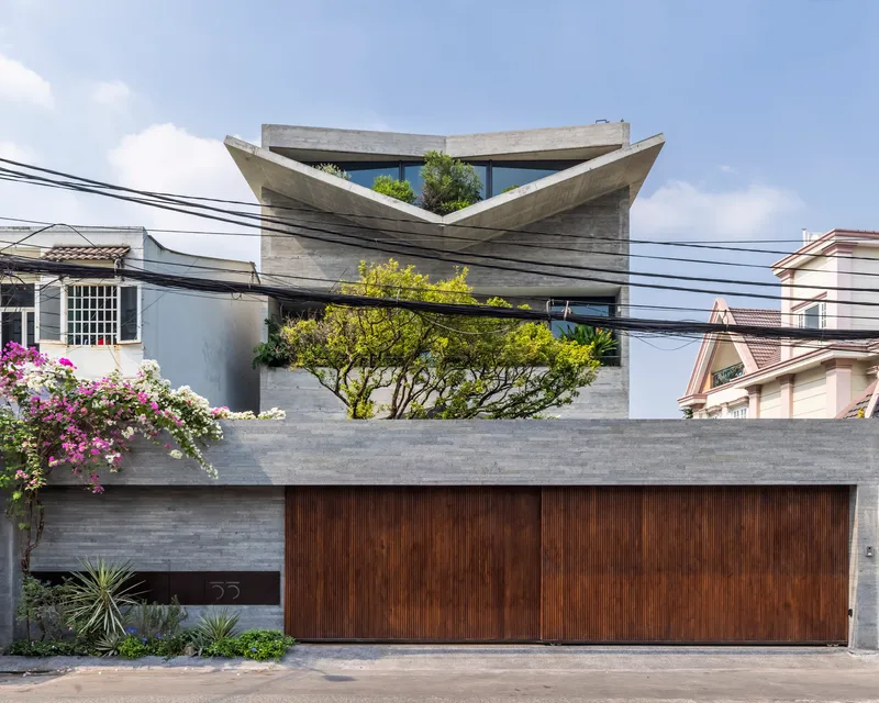 Street view of the board-formed concrete facade with folded roof planes and vertical wood garage door