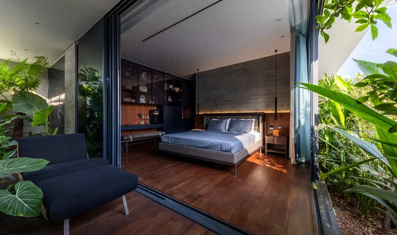 View through folding glass wall from planted terrace into bedroom with dark timber floors