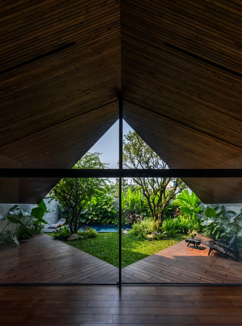 Triangular glazing framing a grass courtyard with lounge chairs and tropical planting at dusk