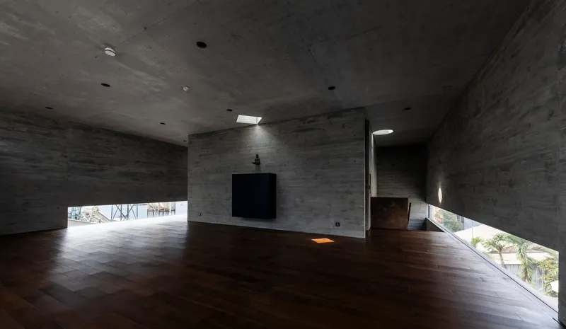 Double-height concrete interior space with dark timber flooring and horizontal strip windows