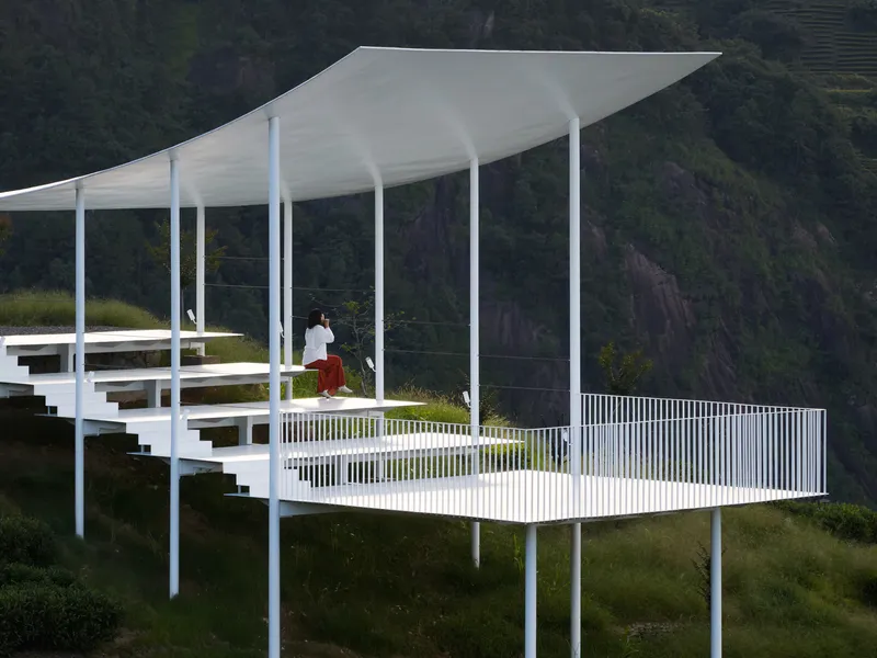 White pavilion deck with benches and vertical railing overlooking valley with visitor in red skirt