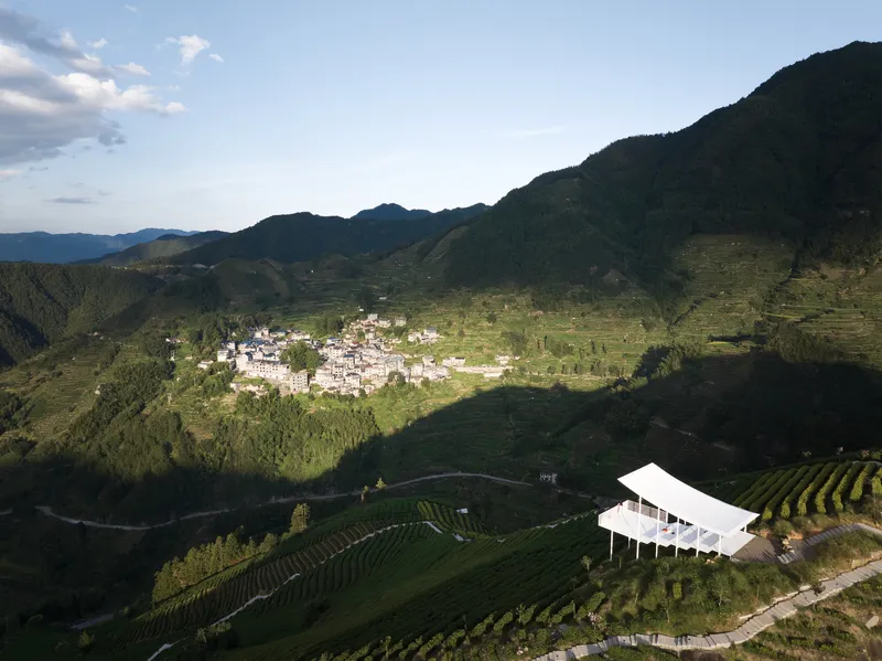 Aerial view of the white canopy structure on terraced hillside overlooking a valley settlement