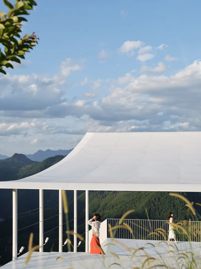 White tensile roof with curved edge over viewing deck where visitors photograph mountain landscape