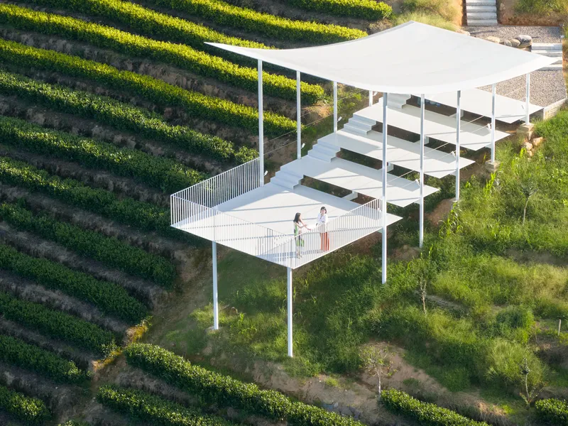 Aerial view of white steel pavilion with terraced platforms and vertical slat railing among planted slopes