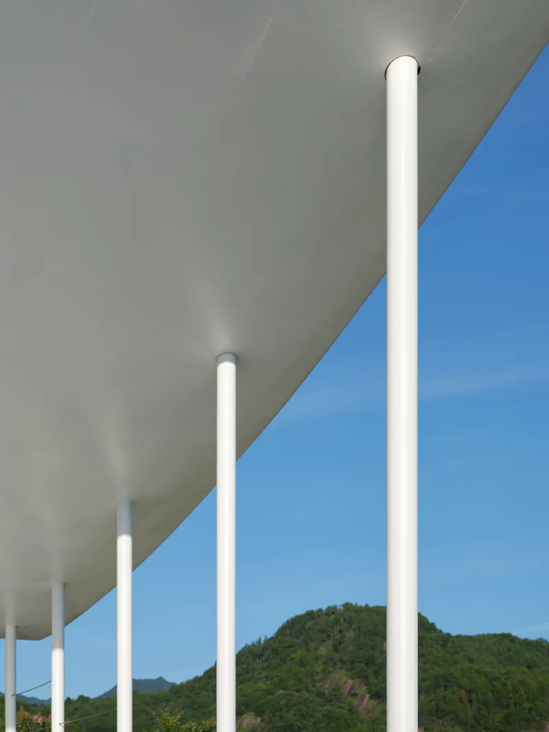 White cylindrical columns supporting a curved canopy against a blue sky with forested hills