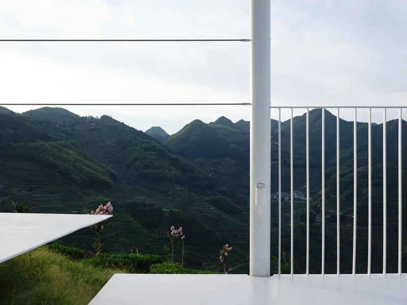 Vertical white railing and horizontal cable rails framing a view of green mountain slopes at dusk