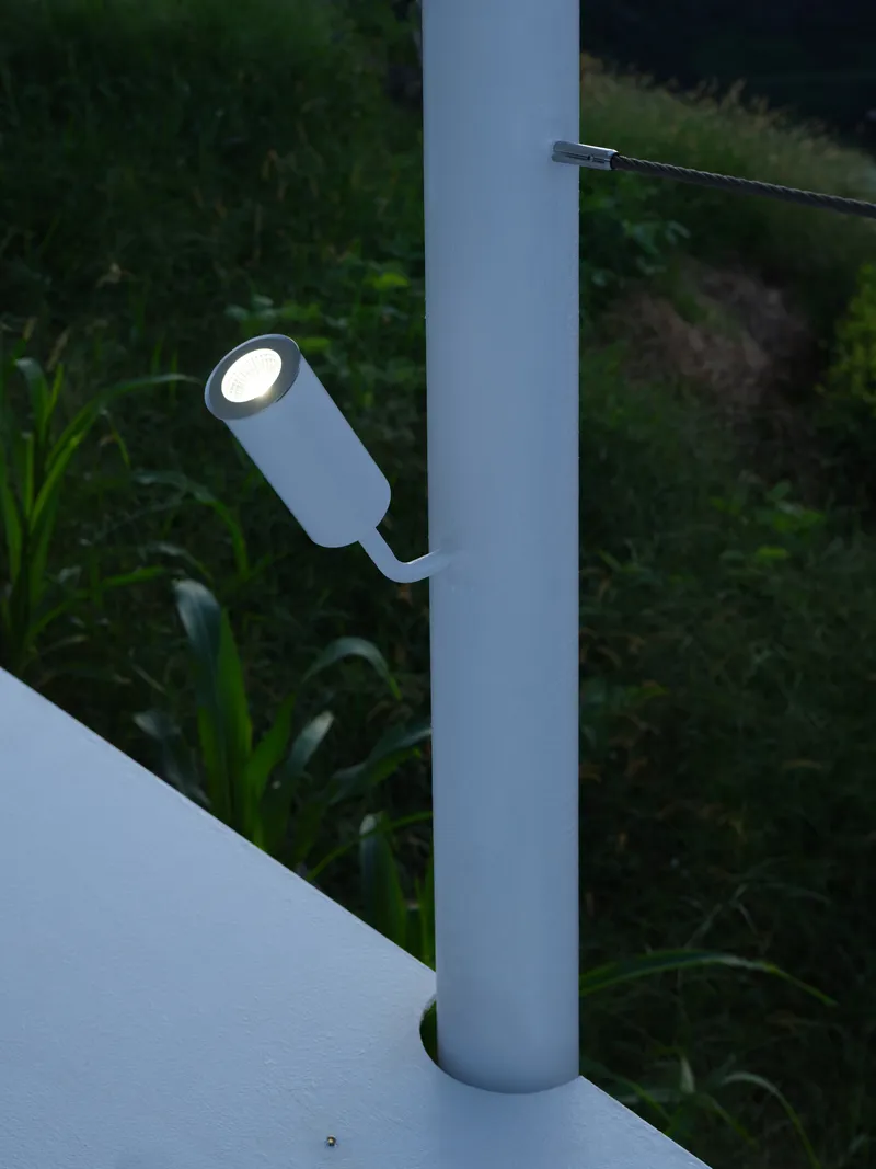 Cylindrical exterior light fixture mounted on a white column at twilight with vegetation beyond