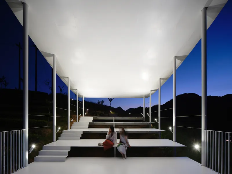 Tiered amphitheater seating under an illuminated canopy with columns at night as two people sit together