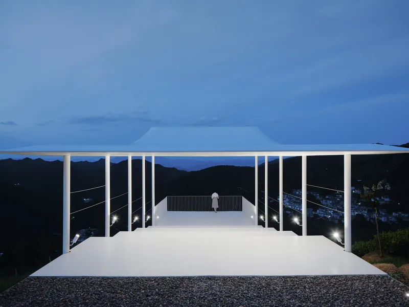 Elevated white pavilion with slender columns and a cantilevered roof at dusk overlooking mountains