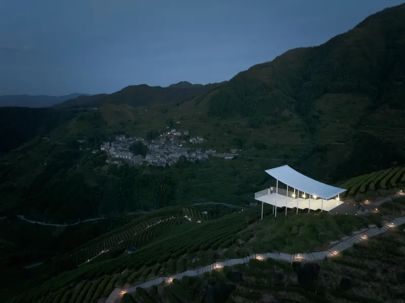 Aerial view of the pavilion perched on terraced tea fields above a hillside village at twilight