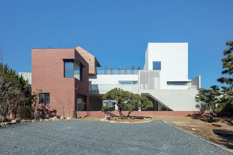 Gravel driveway approaching the clustered volumes of red brick and white stucco under a clear blue sky