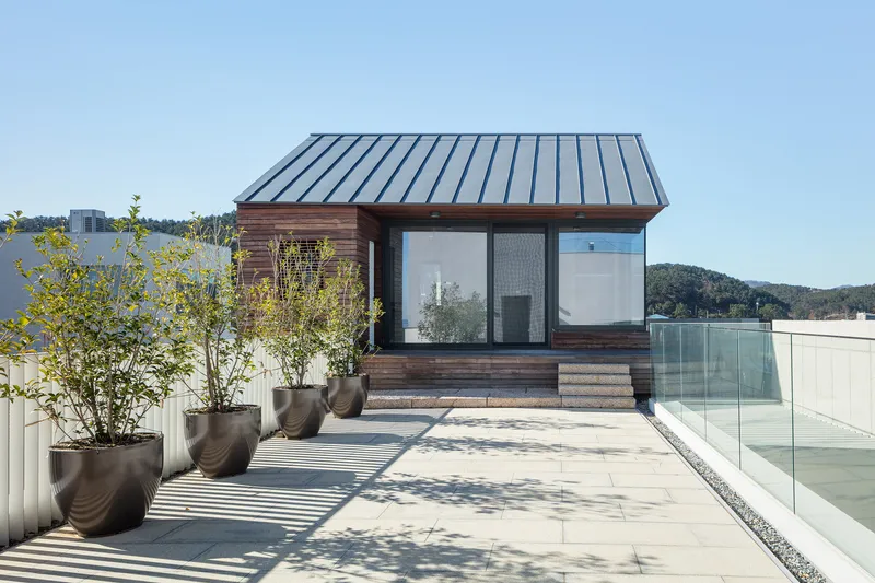 Timber-clad pavilion with standing seam metal roof on a rooftop terrace with glass balustrade