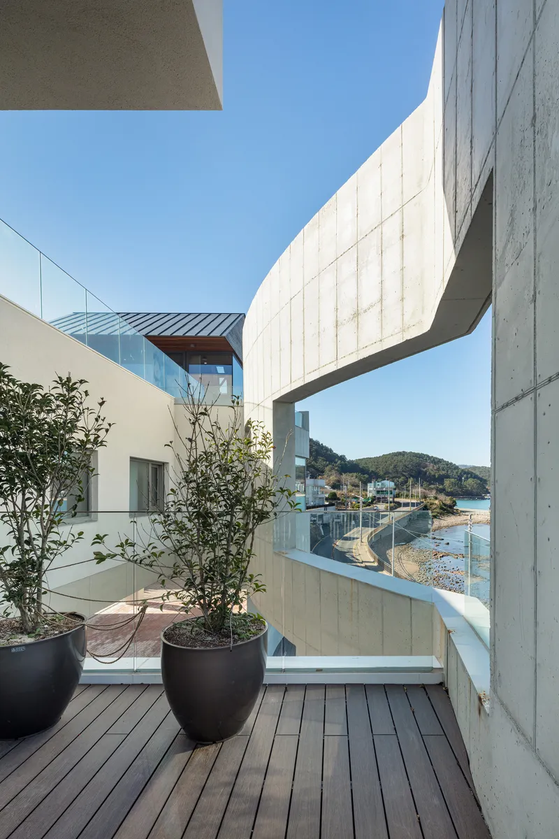 Deck terrace with potted trees overlooking a bridge volume, glass railings, and the distant coastline